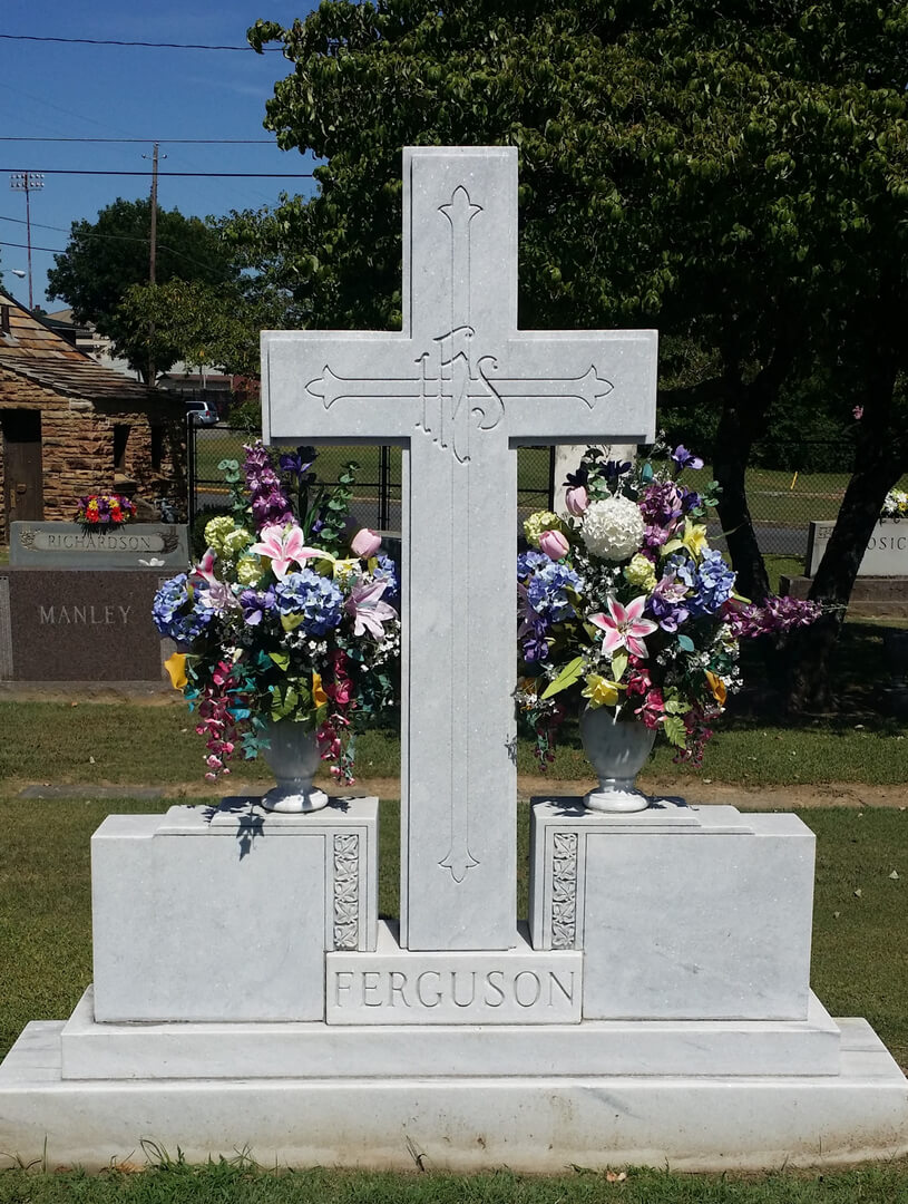 A cross shaped memorial slab with the name Ferguson with flowers