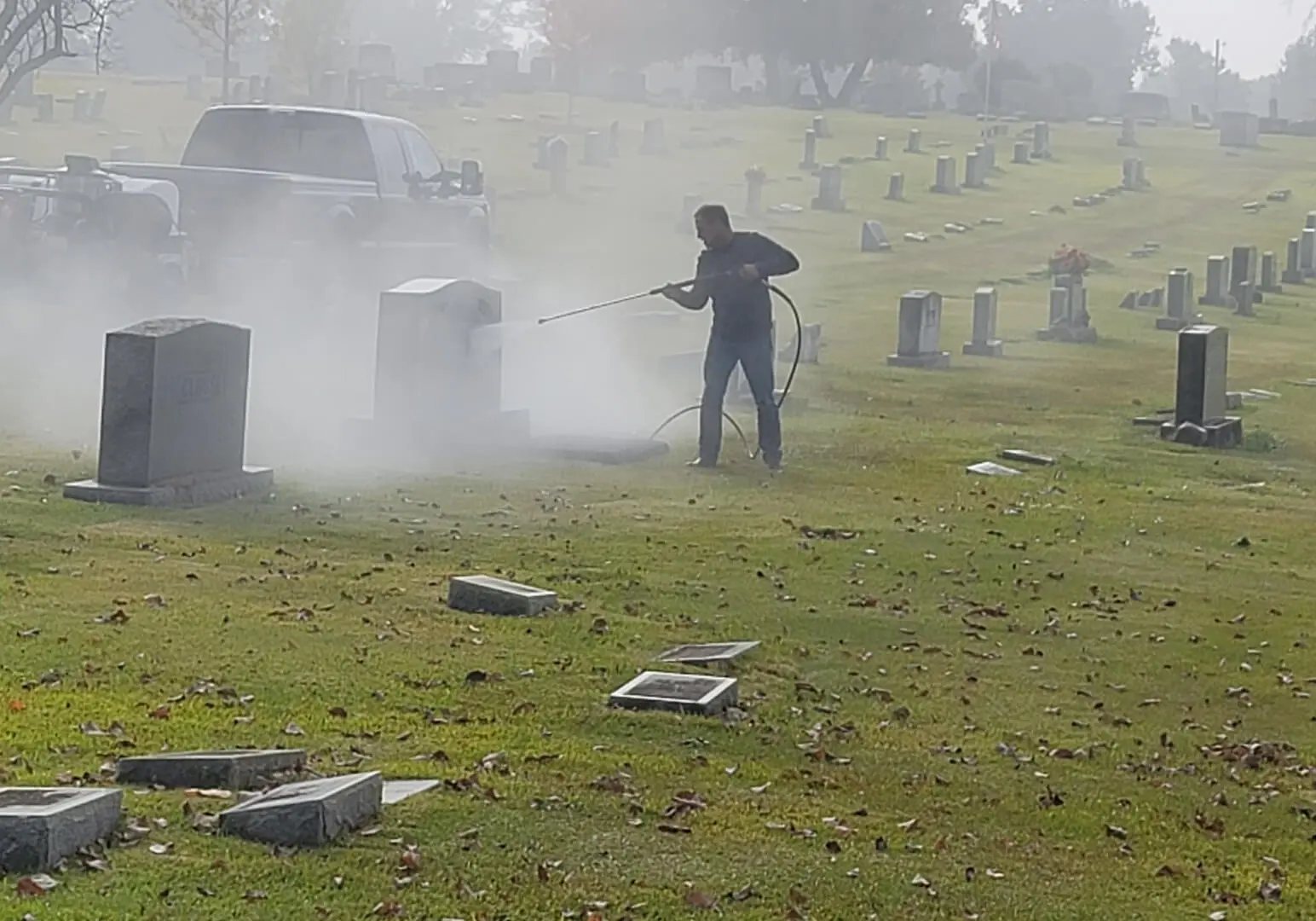 A Man Spraying on a Tombstone to Clean